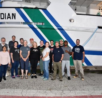 Fifteen people pose in two rose in front of a docked ship Lake Guardian