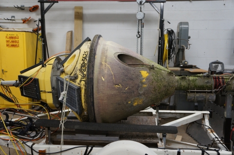 A buoy on a trailer inside a garage. The bottom half of the buoy is covered in dried algae and is completely stained except for a few scratches that show the original color. The upper part is faded from sun-bleaching and has some algae stains too.