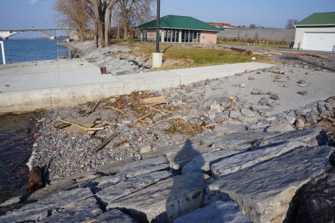 A boat ramp that is mostly filled in with gravel of various sizes, from normal pebble-sized stones to stones the size of someone's head. There is also some woody debris deposited on top of the stones.