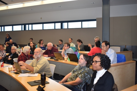 Conference participants taking notes on laptops in a lecture hall.