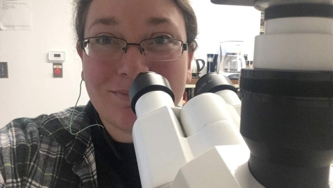 A selfie from a person sitting at a microscope.