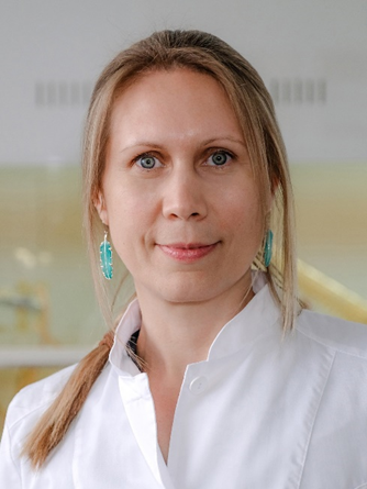 portrait of Olesia Makhutova (Kormilets), a light-skinned person with light and darker blond hair pulled back into a pony tail over the shoulder with some loose hair framing their face, grey eyes, turquoise feather-shaped earrings, and a white collared shirt or lab coat