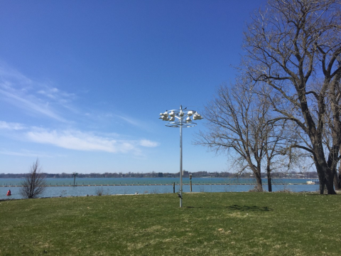 A pole with several round bird houses at the top in a field by some trees and a body of water.