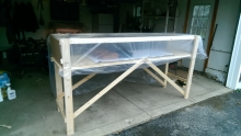 A wooden table frame set up in a garage. There is sheer plastic sheeting stretched over the top part of the frame.