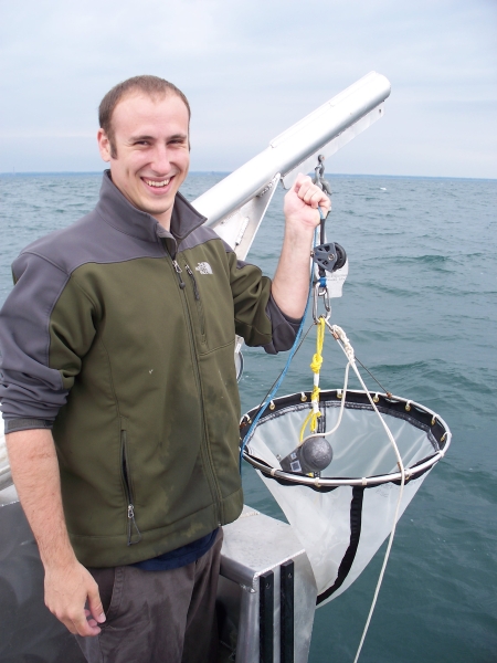 A person smiles and holds up a net on a boat.