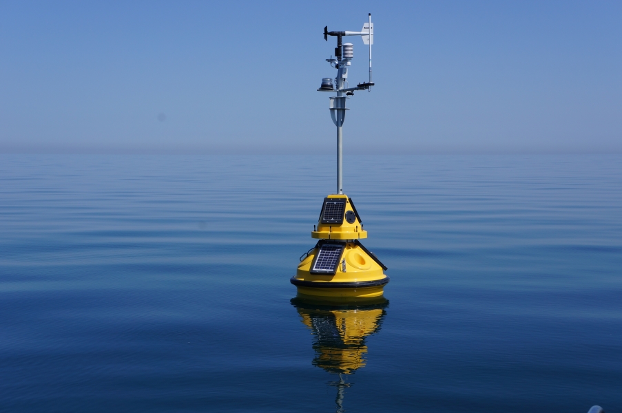 A science buoy with weather instruments on a tall mast floating on calm water