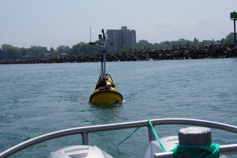 A buoy is being towed behind a boat by a breakwall in a harbor