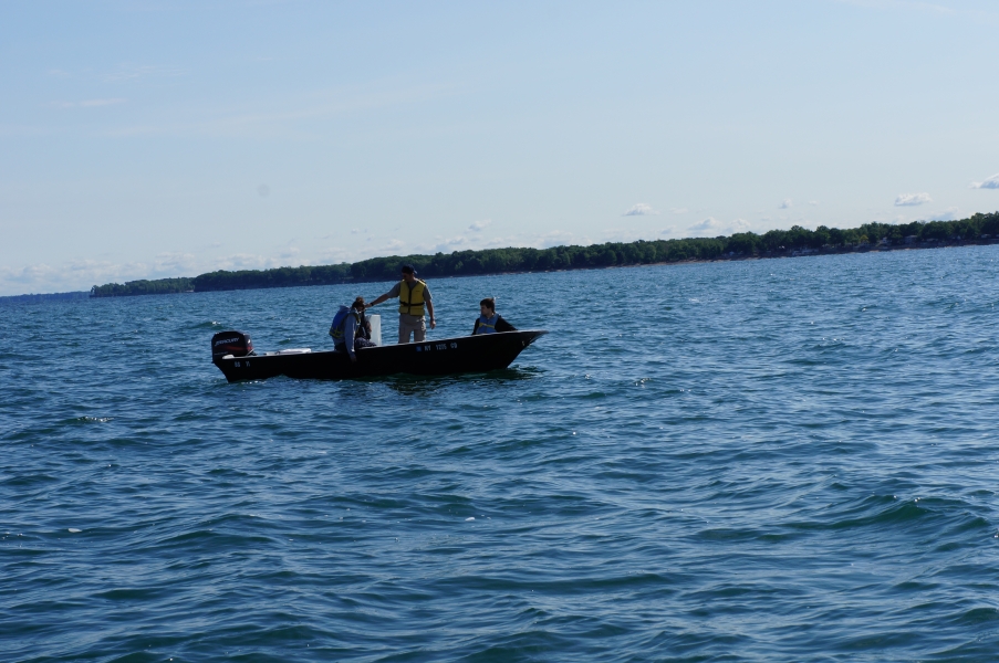 Three people sit on a boat on the water. One is looking at a device in their lap