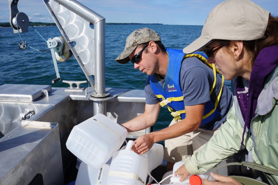 Two people stand in the back of a boat and look at the labels on sample jugs