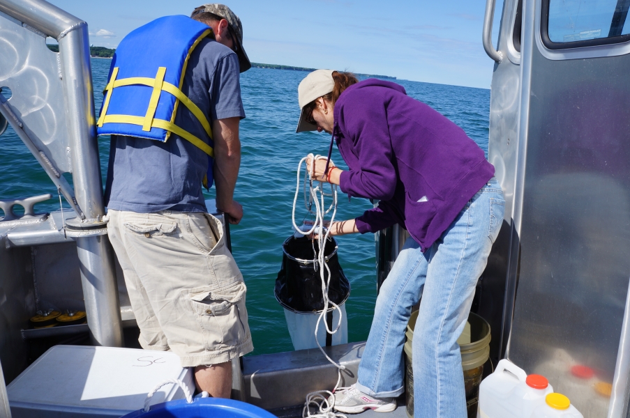 A person holds a conical net over the side of a boat while a second person watches. The first person is checking something in the mouth of the net.