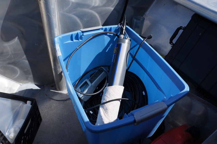 A cylindrical sampling sonde sits in a plastic tub with its cable. Part of it is wrapped with a towel.