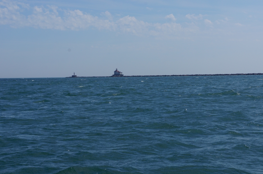 A lighthouse at the end of a pier in the distance, seen from a lake