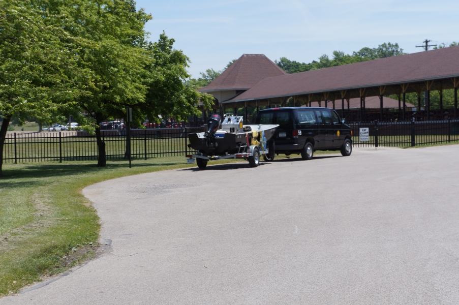 A large van with a boat on a trailer is parked near a picnic structure