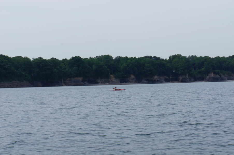 A person in a kayak paddles in front of a short cliff that is unevenly eroded