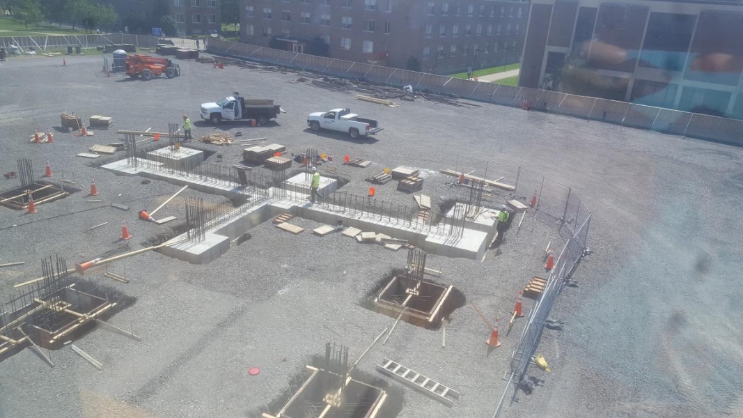 A construction site with large square holes with concrete and rebar in them and the beginning of a wall of a foundation.