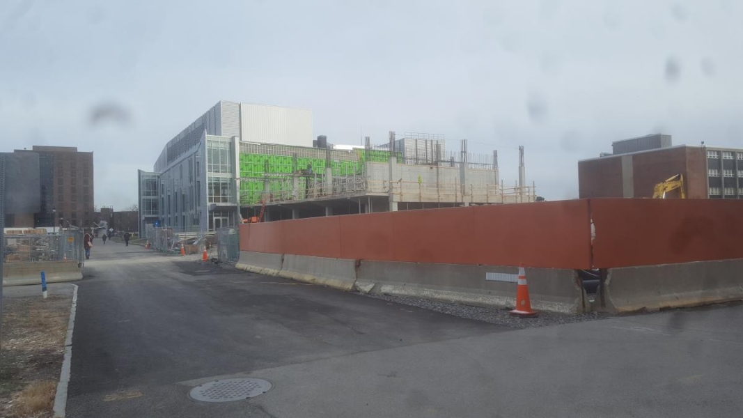 A building under construction with a two story addition with concrete walls and rebar. A fence separates the construction site from the rest of campus.