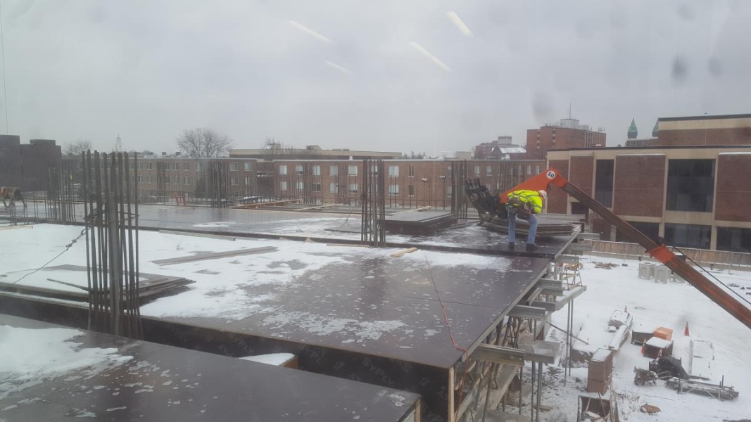 A construction worker supervises as a fork lift places steel plates on the second floor of a building under construction. There is snow on the steel plates that comprise the floor.