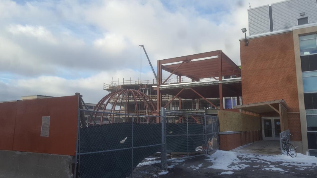 A partially constructed building made of concrete and steel beams . There is a section that is a dome made of steel beams.