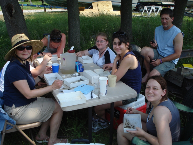 Seven people sit at a table picking through samples in small plastic trays