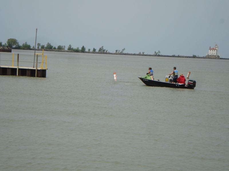 A small boat with a few people on it near a dock. There is a lighthouse in the distance.