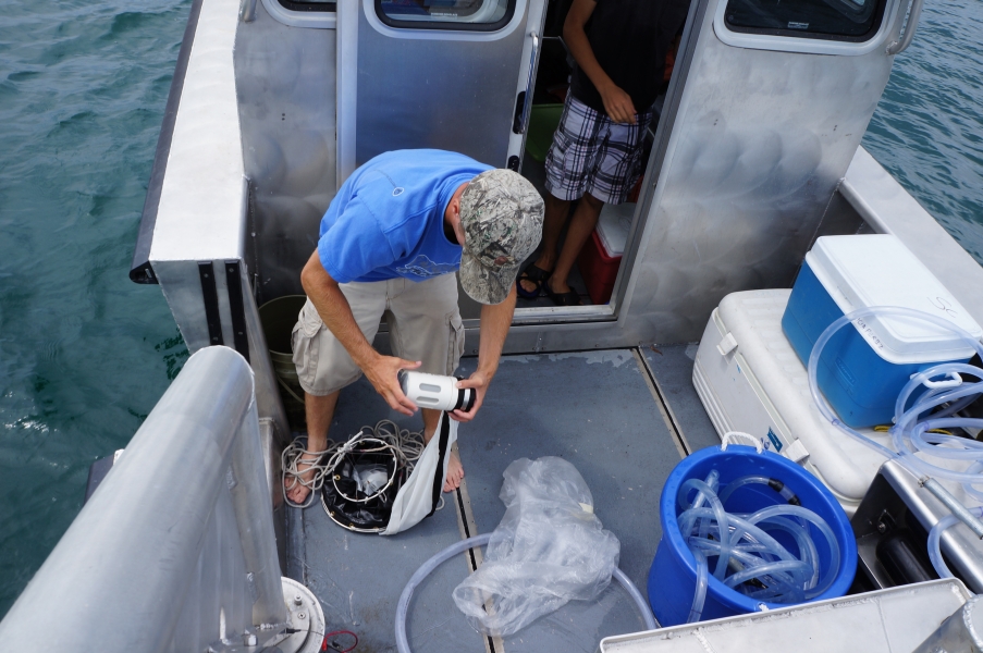 A person on a boat screws a small jar onto the end of a conical net.