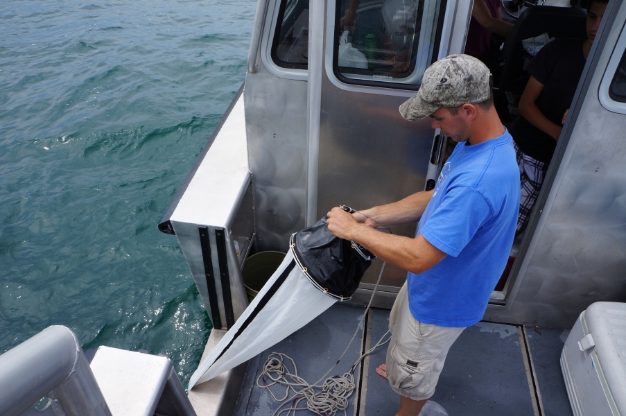 A person holds a conical net over the side of a boat.