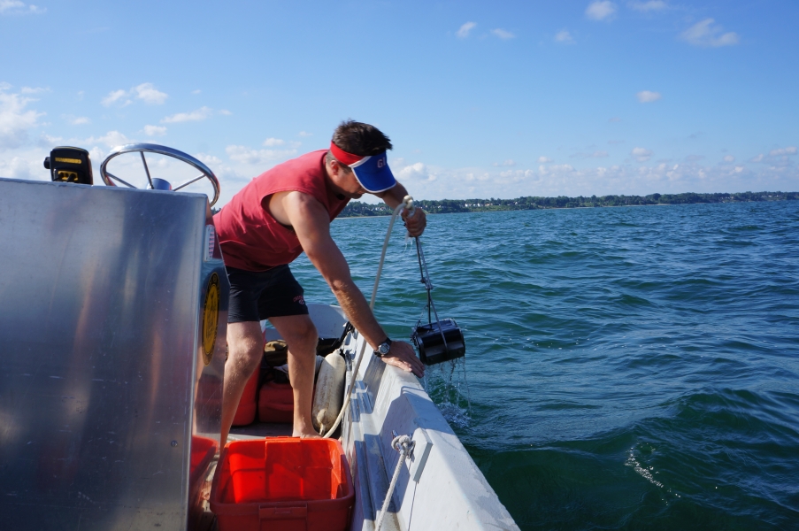 A person pulls a metal grab sampler attached to a rope over the side of a boat