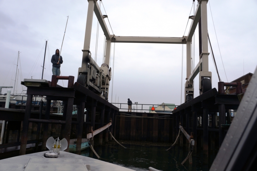 The front of a boat in front of a boat slip with a metal frame and straps in the water