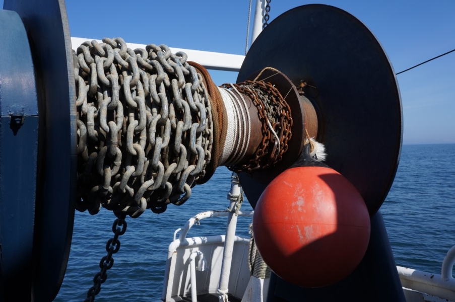 Chain, rope, and an orange float coiled on a large reel on a boat