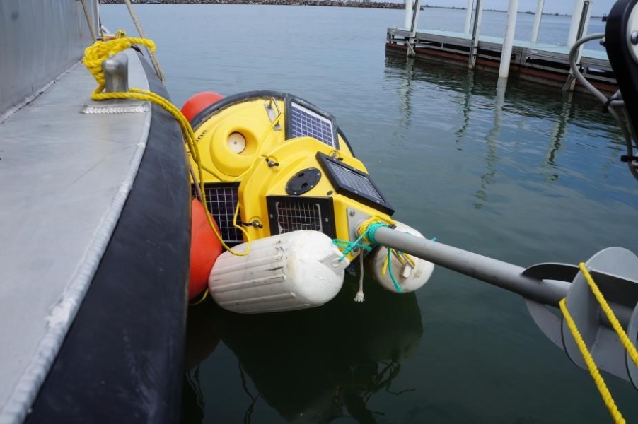 A buoy tied up alongside a boat. The buoy is lying on its side with numerous floats tied to it to keep it in position.