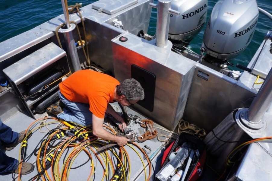 A person in the back of a boat uses a large wrench to attach a rope and chain to some cables.