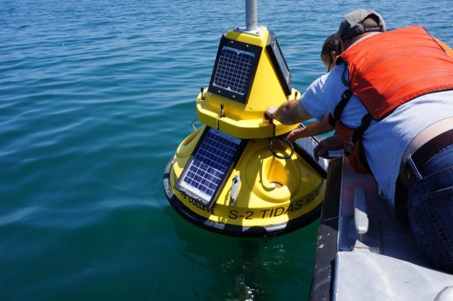 Two people lean over a boat to grab a buoy floating in the water.