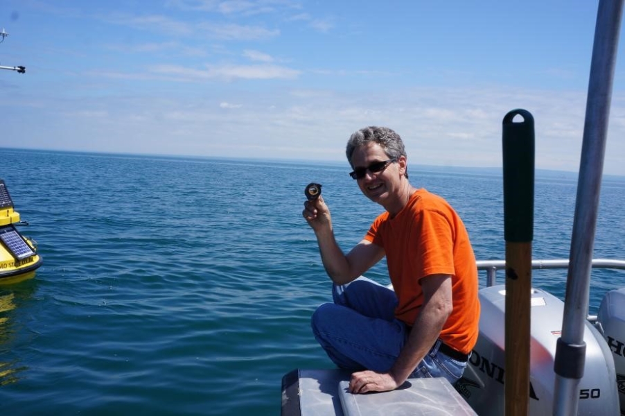 A person sits on the edge of a boat, holding up a roll of tape. A buoy sits in the water next to them.