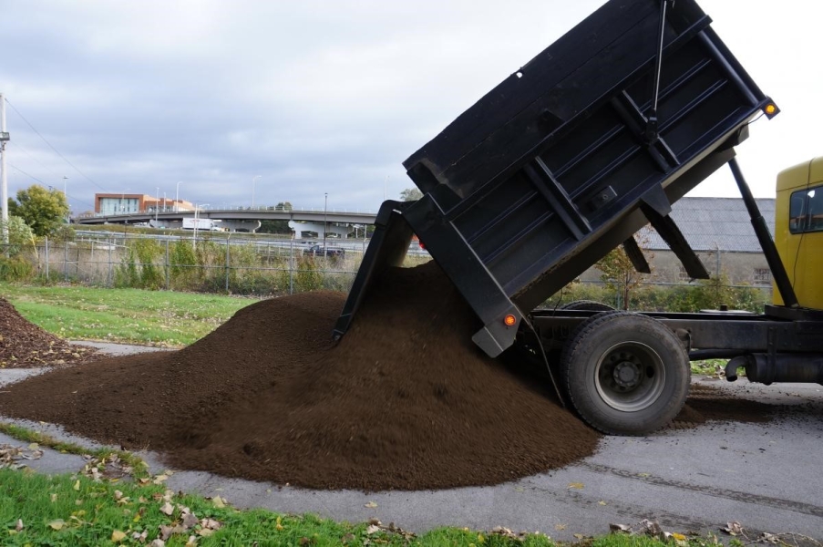 A dump truck pours a pile of dirt onto a roadway.