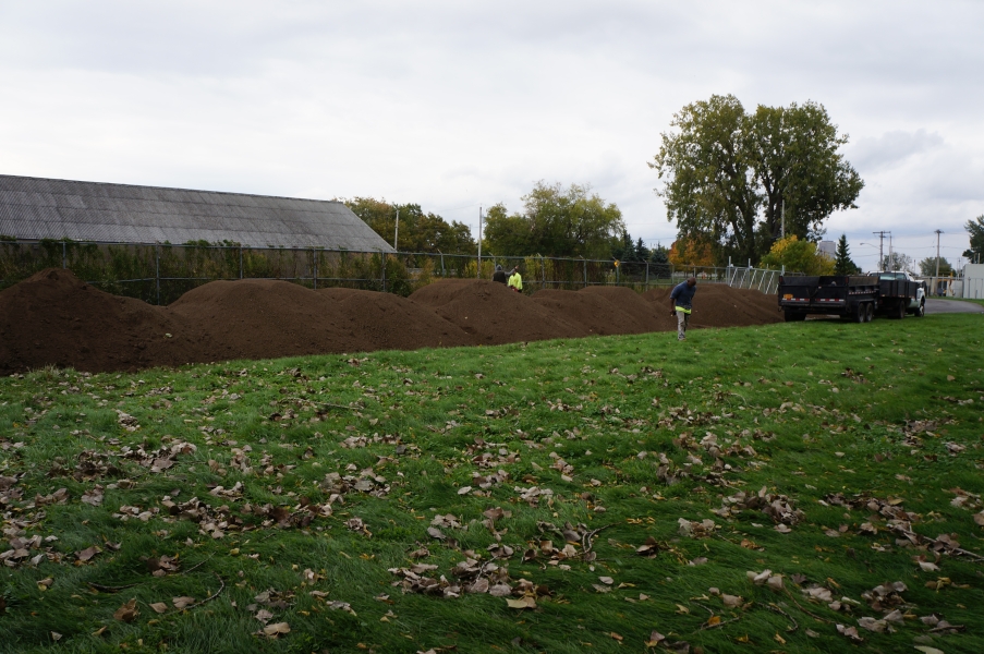 Landscapers work near a line of piles of top soil.