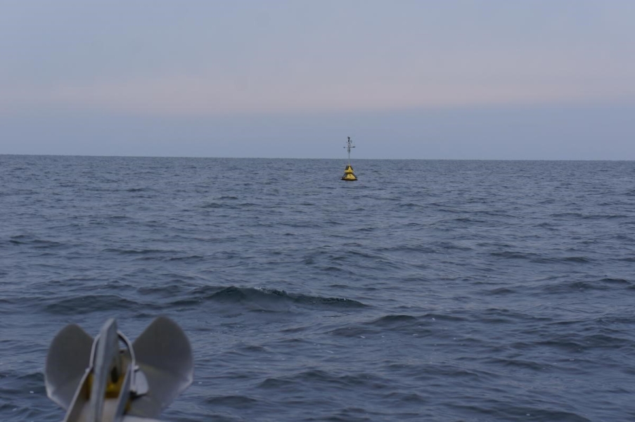 An anchor on the front of a boat approaching a buoy at sea.