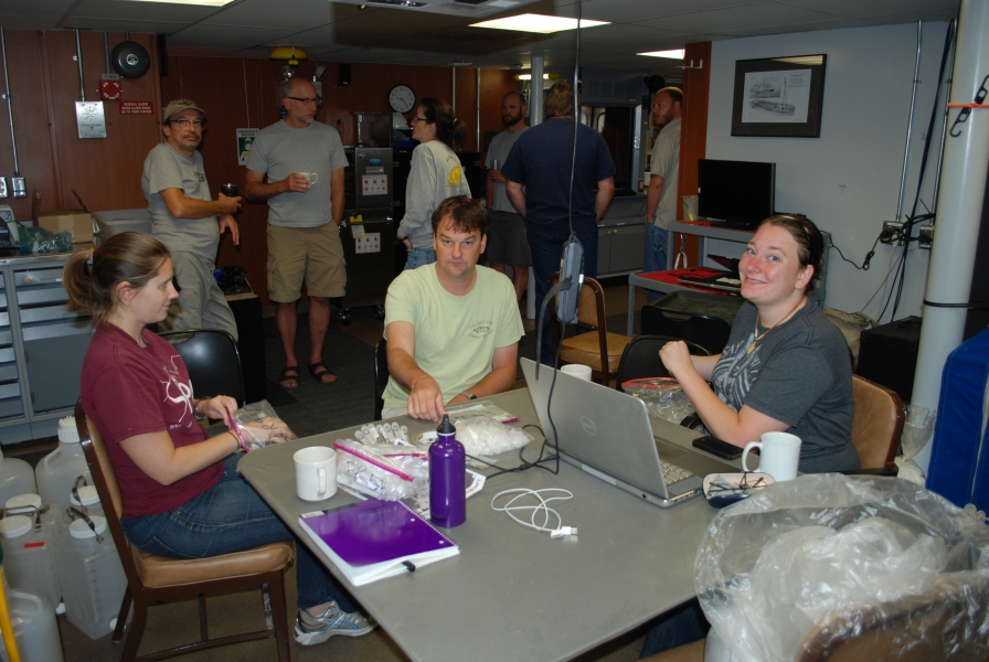 Several people sit or stand inside a lab on a boat.