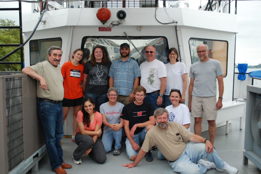 Twelve people pose for a group picture near the wheelhouseof a large boat