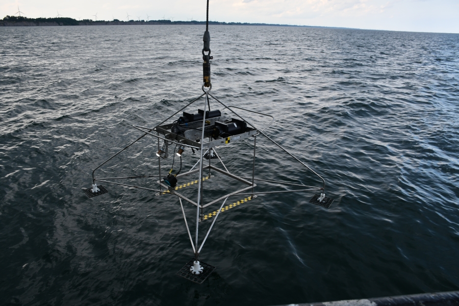 Equipment hanging over a body of water on a cable winch, a metal frame with lights and cameras