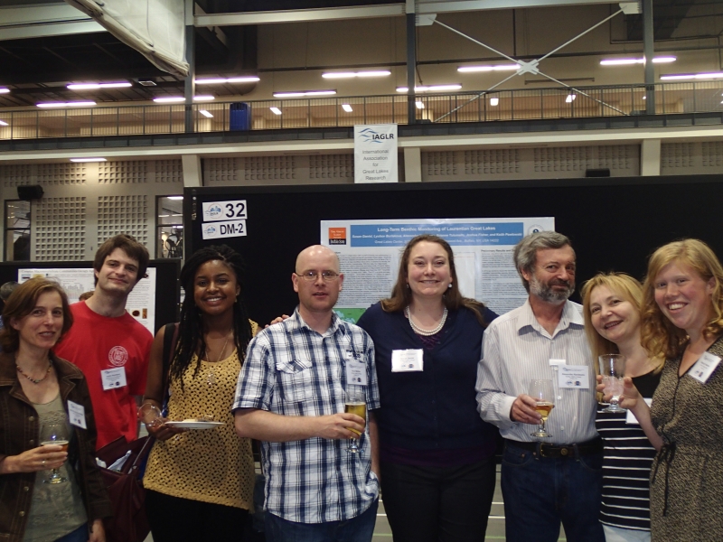 Eight people pose for a picture in front of an academic poster on a board at a conference