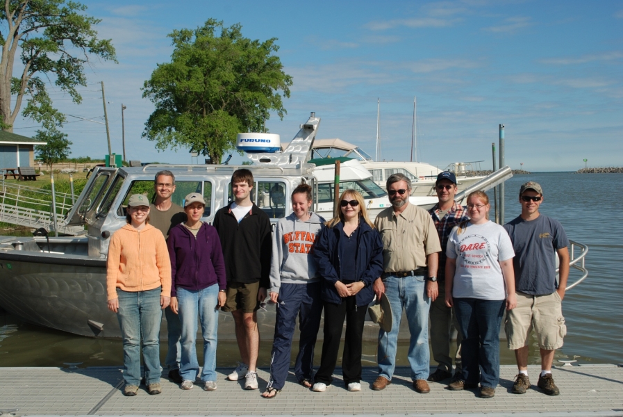 Ten people stand on a dock in front of a boat