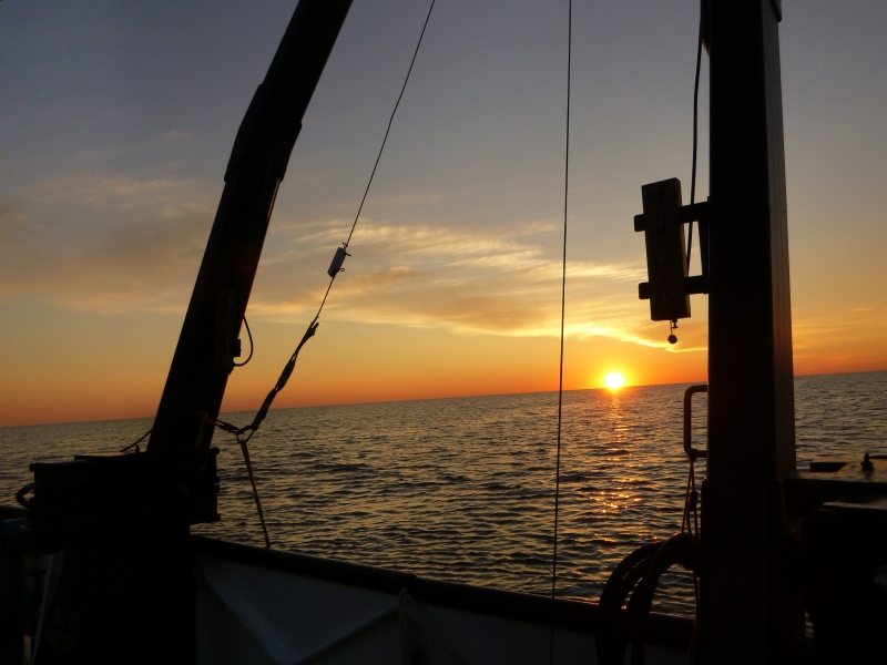 Sunset over the water, seen through the A-frame on a large boat.