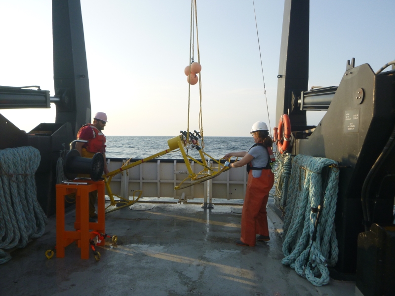 Two people help steady a metal frame as it is lifted off the deck of a large boat by a winch.