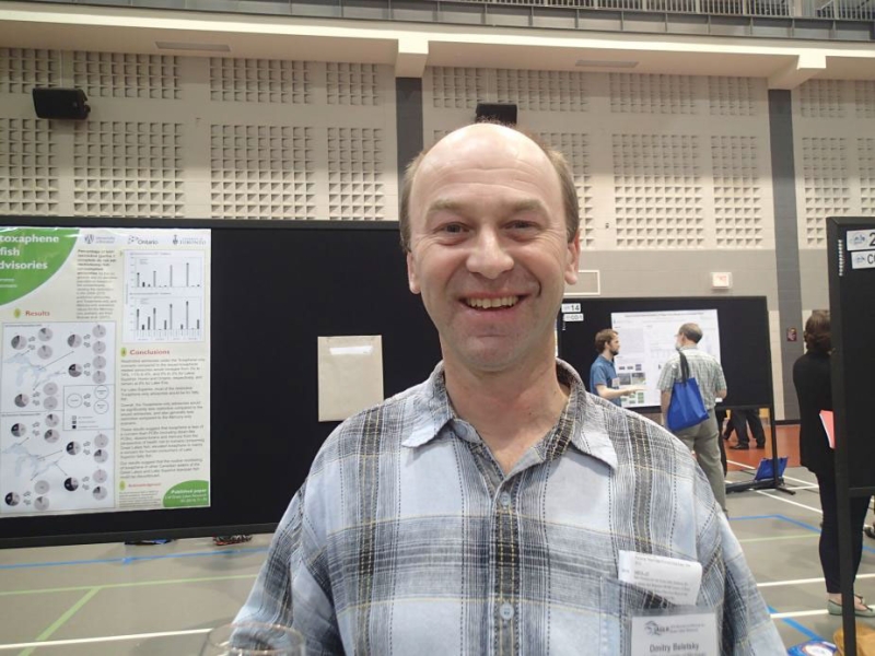 a person stands smiling at the camera in a large room with posters set up on boards