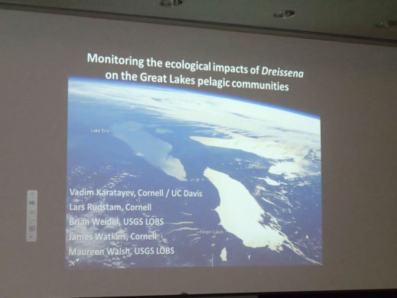 picture of a presentation projected on a screen. There is an aerial photo of large lakes with text that says "Monitoring the ecological impact of Dreissena on the Great Lakes pelagic communities"